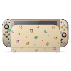 May include: A beige Nintendo Switch console with matching controllers. The console and controllers are decorated with colorful cartoon character graphics. The screen is framed in a bronze color.