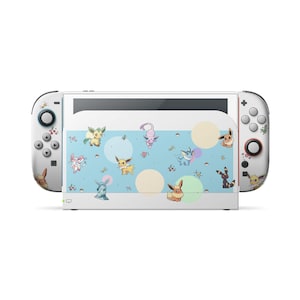 Könnte beinhalten: Eine weiße Videospielkonsolen-Dockingstation und Controller mit einem hellblauen Mittelteil, das mit verschiedenen bunten Evoli-Entwicklungs-Charakteren, kleinen Poké-Bällen, Herzen und zarten Pastellkreisen auf der Oberfläche verziert ist.