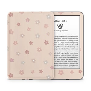 Puede incluir: Un lector electrónico Kindle rosa y beige con un patrón floral en la cubierta. La pantalla muestra el texto "CAPÍTULO 1" y "La Llama de Tar Valon".