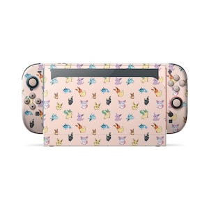 May include: A handheld gaming console featuring a light pink skin with a repeating pattern of various small, colorful cartoon creatures. The design covers the central console unit and both detachable side controllers, displaying multiple character variations.