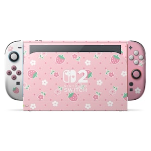 以下が含まれることがあります： イチゴと花の模様が入ったピンク色のNintendo Switchコンソール。Joy-Consは白とピンクで、お揃いのデザインです。画面にはNintendo Switchのロゴが表示されています。