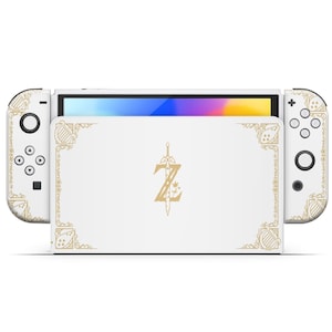 May include: White Nintendo Switch console with a custom design featuring a gold-colored 'Z' with a sword and decorative borders. The console is closed and the screen is off.