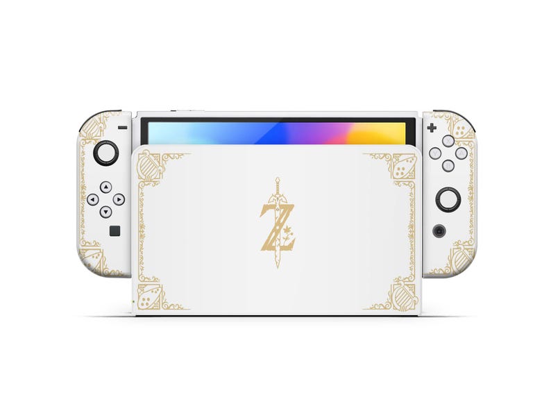 May include: White Nintendo Switch console with a custom design featuring a gold-colored 'Z' with a sword and decorative borders. The console is closed and the screen is off.