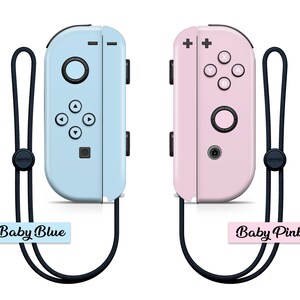 K&ouml;nnte beinhalten: Zwei Nintendo Switch Joy-Con-Controller, einer in Babyblau und einer in Babyrosa, mit schwarzen Handgelenkschlaufen und Etiketten mit der Aufschrift "Baby Blue" und "Baby Pink".