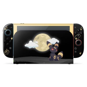 Könnte beinhalten: Eine Nintendo Switch-Konsole mit einem individuellen Design, das einen Cartoon-Umbreon-Charakter, einen Vollmond und Wolken auf schwarzem Hintergrund zeigt. Die Joy-Con-Controller sind schwarz mit goldenen Akzenten.