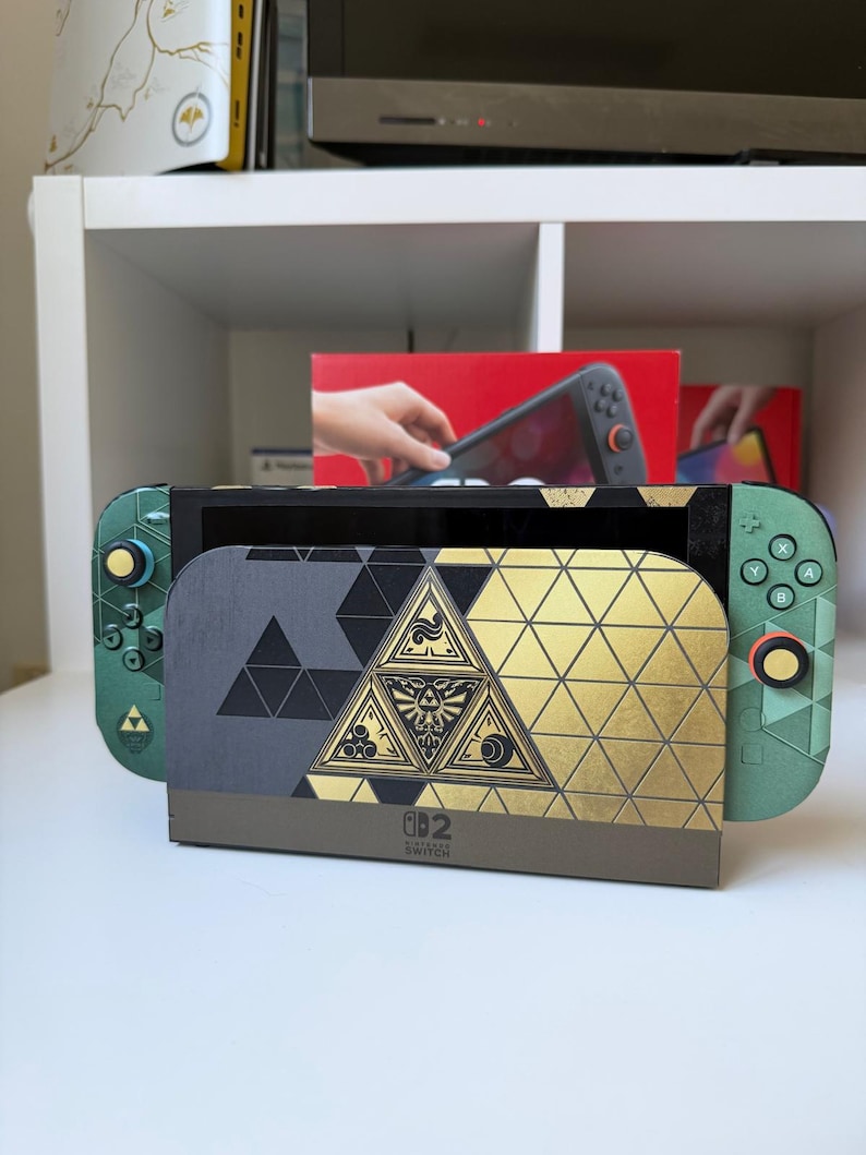 K&ouml;nnte beinhalten: Eine Nintendo Switch Konsole mit einem individuellen Skin in gr&uuml;nem, schwarzem und goldenem geometrischem Muster. Die Dockingstation zeigt ein zentrales dreieckiges Emblem mit feinen Linien, und die Joy-Con Controller haben passende Akzente.