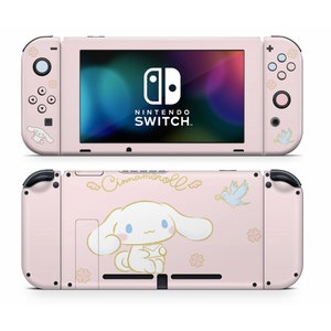 May include: Pink Nintendo Switch console with a Cinnamoroll character design. The console features a white dog with floppy ears and a blue bird. The text "Cinnamoroll" is written in cursive on the back of the console.