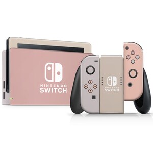 May include: A pink and beige Nintendo Switch console with two Joy-Con controllers. The console has the Nintendo Switch logo and the text "NINTENDO SWITCH". The Joy-Con controllers have the Nintendo Switch logo and the text "NINTENDO SWITCH".