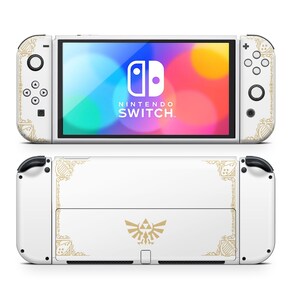 May include: White Nintendo Switch console with a gold and white Zelda themed design. The console has a gold border and a Triforce symbol in the center. The screen displays the Nintendo Switch logo.