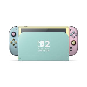 May include: A Nintendo Switch console featuring a light blue left Joy-Con with gold buttons and a pink right Joy-Con with a gold joystick. The dock is light blue and displays the text Nintendo Switch with a heart icon replacing the letter O.