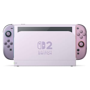 Peut inclure: Une console Nintendo Switch lavande avec des manettes Joy-Con assorties. La console présente le logo Nintendo Switch et un motif de cœur stylisé. Les manettes sont dans des tons lavande et rose, avec des boutons et des joysticks noirs.