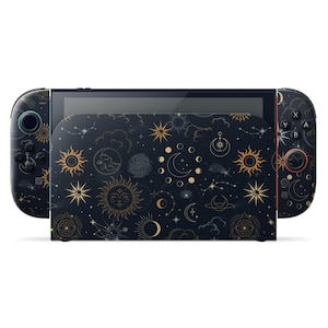 Op de afbeelding: Een zwarte en gouden Nintendo Switch-console en -dockingstation met een hemels thema. Het ontwerp toont zonnen, manen, sterren en sterrenbeelden op een donkere achtergrond. De controllers en het dockingstation hebben een bijpassend patroon.