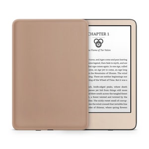 Może przedstawiać: Czytnik Kindle Paperwhite w kolorze beżowym z brązową osłoną. Na ekranie wyświetla się tekst "ROZDZIAŁ 1" i "Płomień Tar Valon".