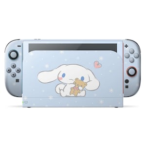 以下が含まれることがあります： 水色のNintendo Switchコンソール。漫画のキャラクターデザインが特徴です。コンソールは、白い雪の結晶とテディベアを抱きしめている漫画のキャラクターが描かれた水色の背景です。コントローラーは、白いボタンが付いた水色です。