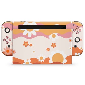 Könnte beinhalten: Eine rosa, orange und weiße Nintendo Switch Konsolenhaut mit einem Blumenmuster. Die Haut zeigt ein sich wiederholendes Muster aus Gänseblümchen und Wellenlinien.