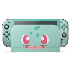 以下が含まれることがあります： フシギダネのデザインが施された、ティール色のNintendo Switchドックとコントローラー。ドックにはピンクの目と笑顔の口をしたフシギダネの顔があります。コントローラーには緑色のボタンと迷彩柄があります。