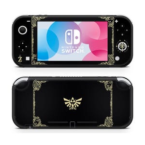 Puede incluir: Consola Nintendo Switch Lite negra con detalles dorados y temática Zelda. La pantalla muestra el logotipo de Nintendo Switch. La parte trasera de la consola presenta el escudo de Zelda. La consola tiene un diseño elegante y moderno.
