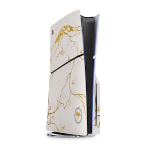 Peut inclure: Console PlayStation 5 blanche avec un motif de carte dor&eacute;. La console pr&eacute;sente une bande noire et un &eacute;clairage bleu. Le design comprend un logo et une illustration de montagne.