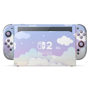 Peut inclure: Une console Nintendo Switch avec un motif de nuages pastel. Les manettes Joy-Con et la console présentent une palette de couleurs bleu clair et blanc avec un motif de nuages et d'étoiles. L'écran affiche le logo Nintendo Switch.