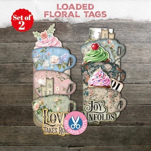May include: A set of two floral tags in the shape of stacked teacups. The tags feature floral patterns, decorative elements, and the words "LOVE TAKES ROOT" and "JOY UNFOLDS". Each tag is topped with a cupcake-like design.