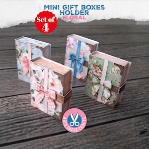 May include: A set of 4 mini gift boxes holder floral, featuring rectangular paper boxes with various floral patterns, decorative bows, and corner accents. The boxes are arranged in a group, each displaying distinct color palettes including blue, pink, and green floral designs with ribbon details.