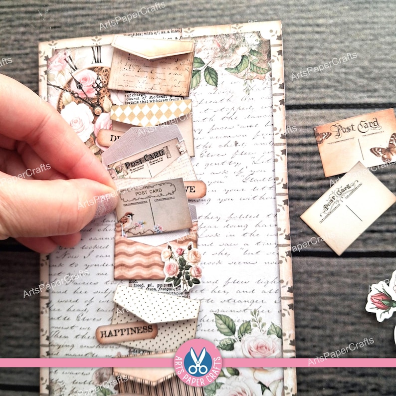 May include: A handmade scrapbook page with a vintage aesthetic. The page features small paper envelopes, postcards, and decorative elements like roses and a clock. The word "HAPPINESS" is visible on one of the envelopes.