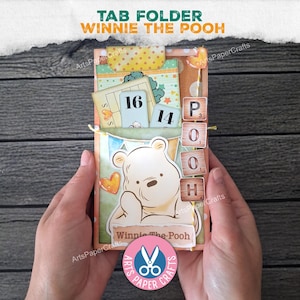 May include: A handmade tab folder featuring Winnie the Pooh. The folder has a light orange background with a Winnie the Pooh illustration, the text "Winnie the Pooh", and the word "POOH" spelled out with wooden tiles. The folder also has a tab with the text "TAB FOLDER".