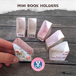May include: Six miniature paper book holders with various floral and patterned designs. Each holder features an open top, slanted sides, and a small rectangular label plate on the front. The text MINI BOOK HOLDERS is printed at the top.