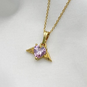 Puede incluir: Un collar de cadena dorada con un colgante de coraz&oacute;n rosa con alas.