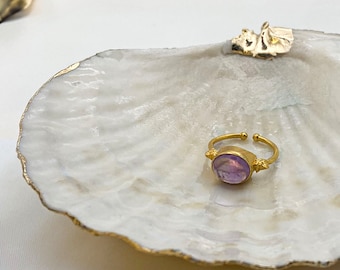 May include: A gold ring with a purple gemstone set in a white seashell dish.