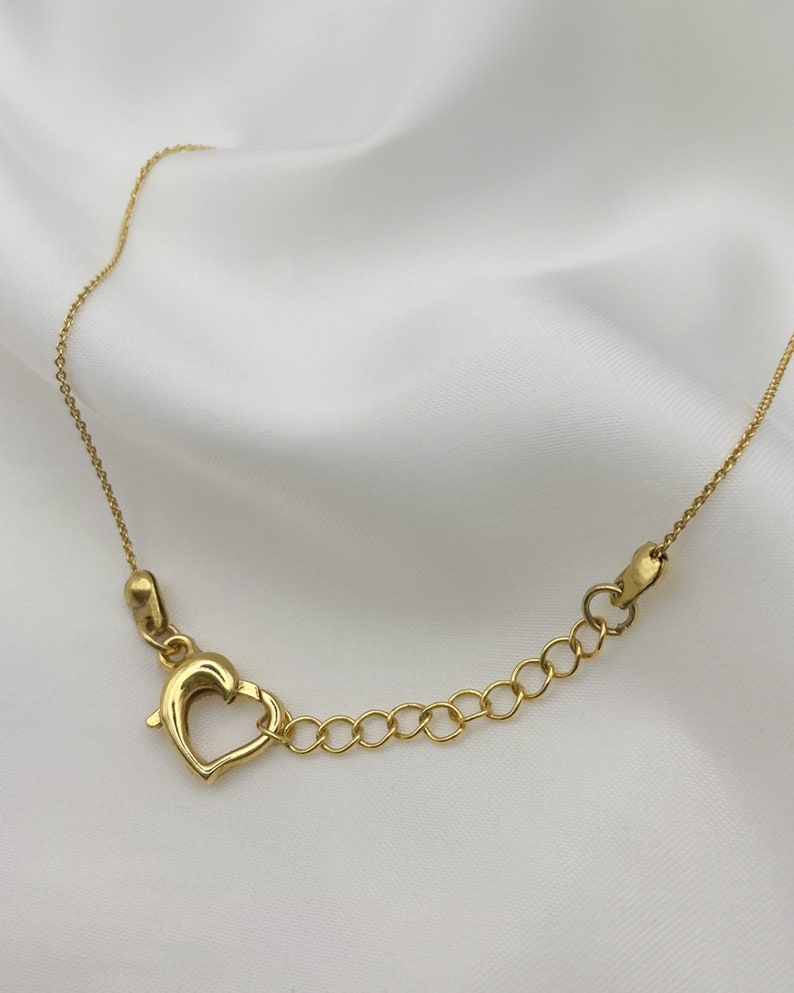 Puede incluir: Un collar de cadena de oro con un cierre en forma de coraz&oacute;n.