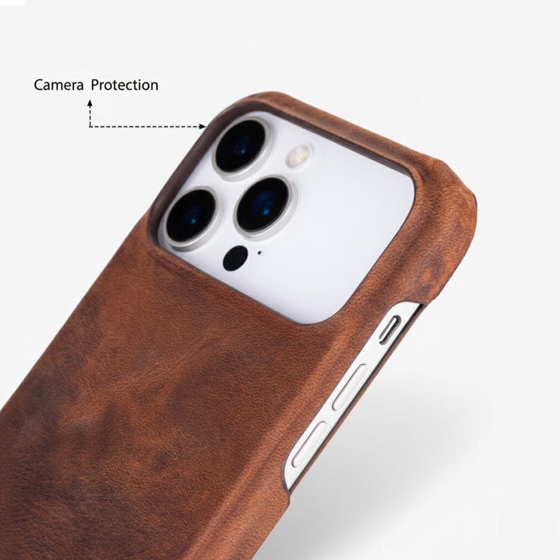 May include: Close-up of a brown leather phone case with camera protection. The case has a textured surface and a snug fit around the phone's camera and buttons. The phone's camera lenses are visible.