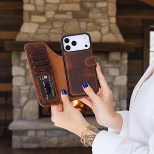 May include: Brown leather phone case with card slots. The case is open, revealing the phone and card slots. The phone has a black frame and a white back. The case has a magnetic closure.