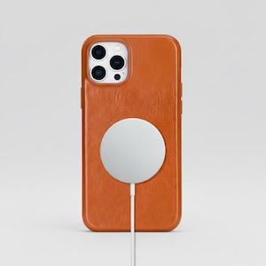 May include: An orange leather phone case with a white circular charger attached. The phone case has a textured surface and a camera cutout. The charger is connected with a white cable.