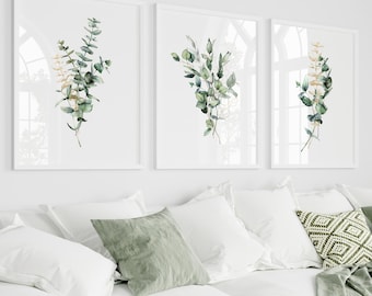 Può includere: Tre stampe botaniche incorniciate con foglie di eucalipto ad acquerello nei toni del verde e del bianco sono appese sopra un divano bianco con cuscini e una coperta verde. La stanza ha pareti bianche e una tenda bianca.