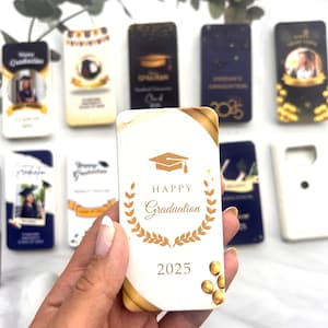 Può includere: Un biglietto bianco con dettagli dorati e un design di cappello di laurea dorato. Il biglietto dice "Happy Graduation 2025" e ha una corona di alloro intorno al testo.