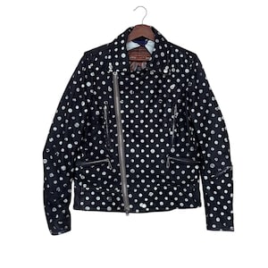 May include: Black leather jacket with white polka dots, featuring a classic asymmetrical zip closure, multiple zippered pockets, and a notched lapel. The jacket is hanging on a wooden hanger.