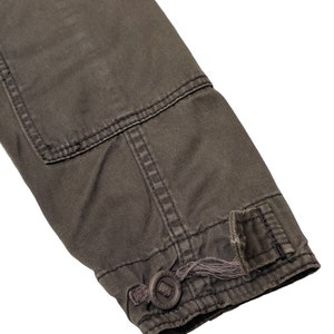 Puede incluir: Primer plano del pu&ntilde;o de una chaqueta gris oscuro con un bot&oacute;n y un lazo para ajustar el ajuste.