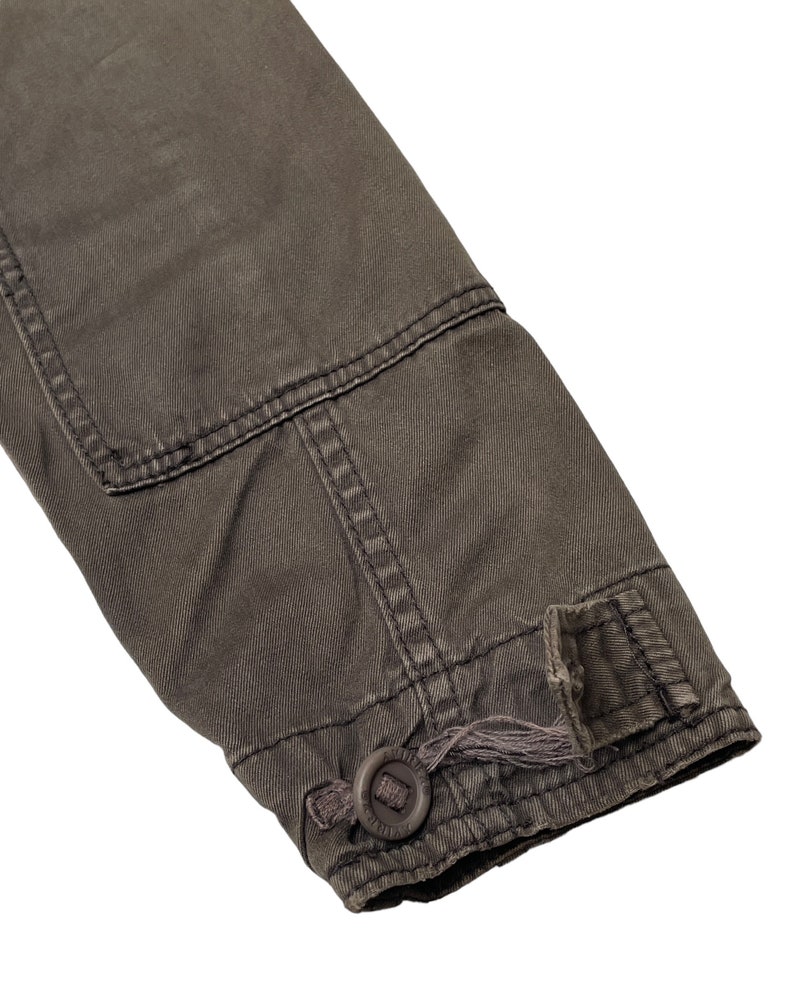 Puede incluir: Primer plano del pu&ntilde;o de una chaqueta gris oscuro con un bot&oacute;n y un lazo para ajustar el ajuste.