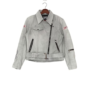 May include: A grey leather motorcycle jacket with a black zip and belt. The jacket has a red and white patch that says "Simpson" on the right sleeve and a black and white patch on the left sleeve.
