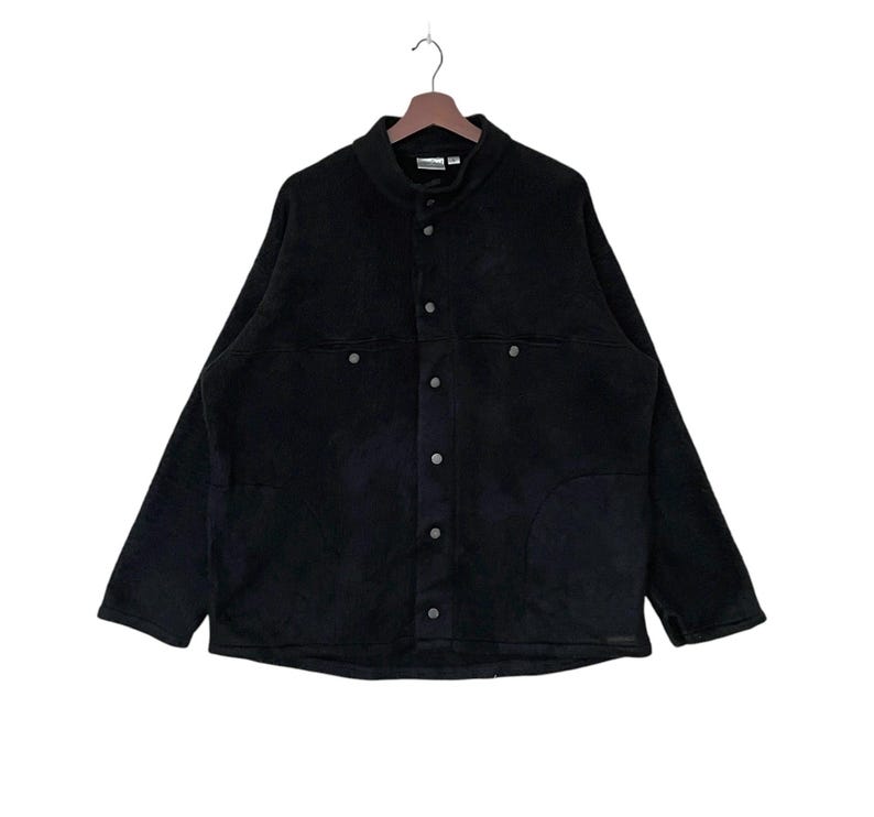 May include: A black fleece jacket with a button-up front and two large pockets. The jacket has a stand-up collar and long sleeves.