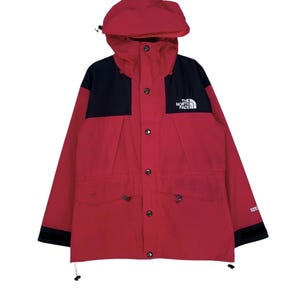 May include: A red and black North Face jacket with a hood and a button closure. The jacket has a logo on the left chest that says "The North Face" and "Gore-Tex" on the right sleeve.