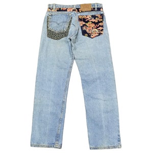 Może przedstawiać: Jasnoniebieskie dżinsy z naszywką z kwiatowym wzorem na tylnej prawej kieszeni i naszywką z czarno-białym wzorem na tylnej lewej kieszeni.