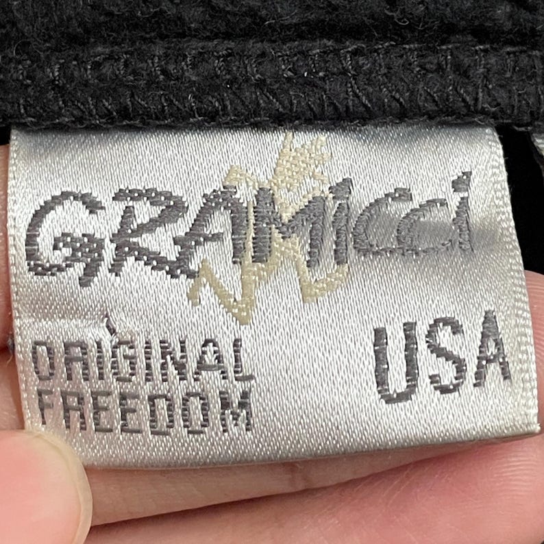 May include: A white tag with black text that reads "GRAMICCI" in a stylized font. Below the brand name, it says "ORIGINAL FREEDOM" and "USA".