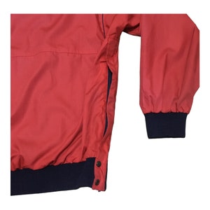 May include: A red jacket with a navy blue zipper and cuffs. The jacket has a snap closure at the bottom.