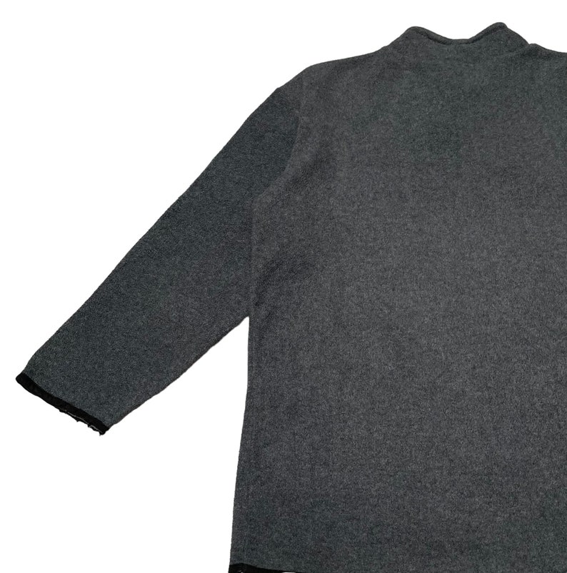 May include: A gray long-sleeved sweater with a mock neck collar. The sweater has a ribbed texture and a slightly distressed hem.