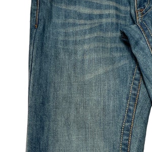 May include: A pair of blue denim jeans with a distressed look. The jeans have a light wash and a faded appearance. The jeans have a classic five-pocket style with a small pocket on the right side of the front.