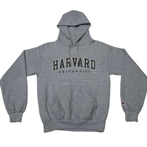 以下が含まれることがあります： グレーのフード付きスウェットシャツに、黒と金の文字で「ハーバード大学」と書いてあります。