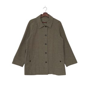 May include: Olive green button-down jacket with a collared neckline and long sleeves. The jacket has a classic design with a button closure and two front pockets. It is hanging on a wooden hanger against a white background.