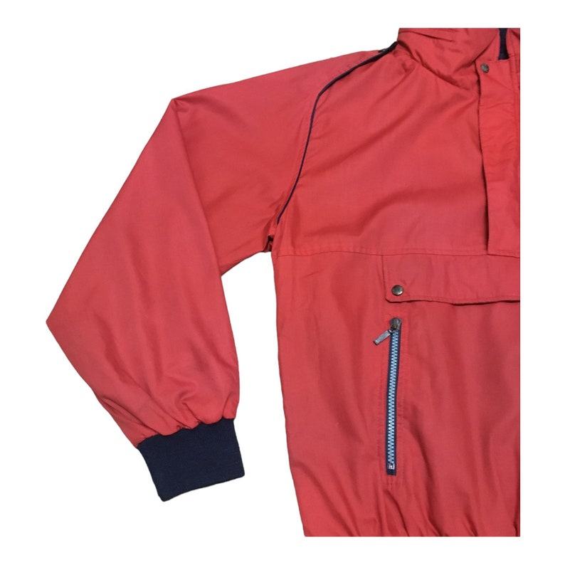 May include: A red jacket with a zippered pocket and a navy blue trim around the collar and cuffs.